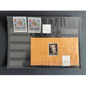 Two Liechtenstein stamps with coats of arms on a dark display page; below is a brown envelope with a black-and-white portrait stamp and small price notes nearby.