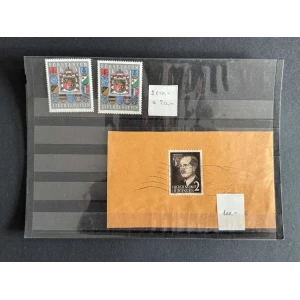 Two Liechtenstein stamps with coats of arms on a dark display page; below is a brown envelope with a black-and-white portrait stamp and small price notes nearby.