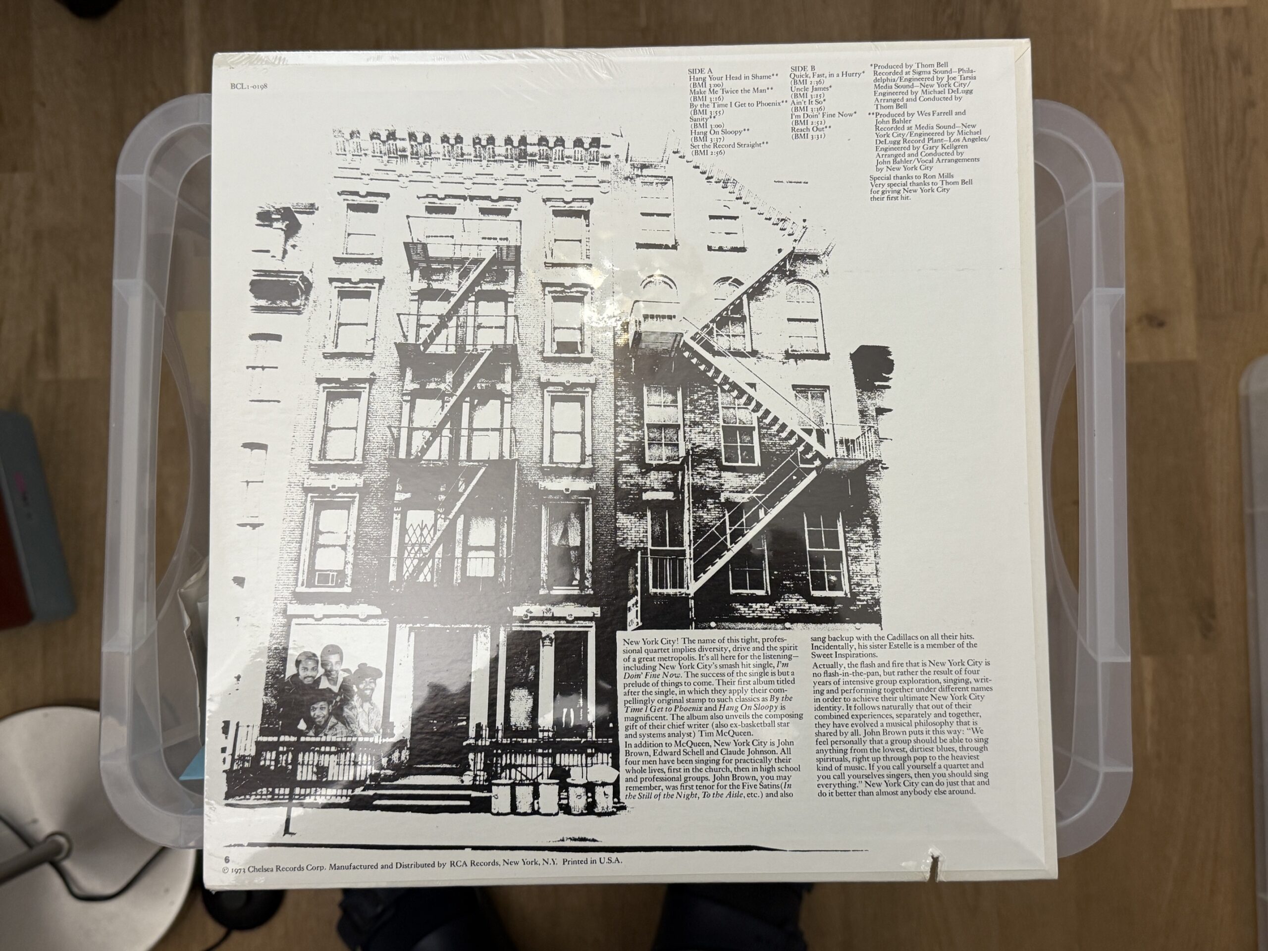 Back cover of a vinyl record showing a black-and-white city apartment building with external fire escapes and a small group photo in the lower-left corner.