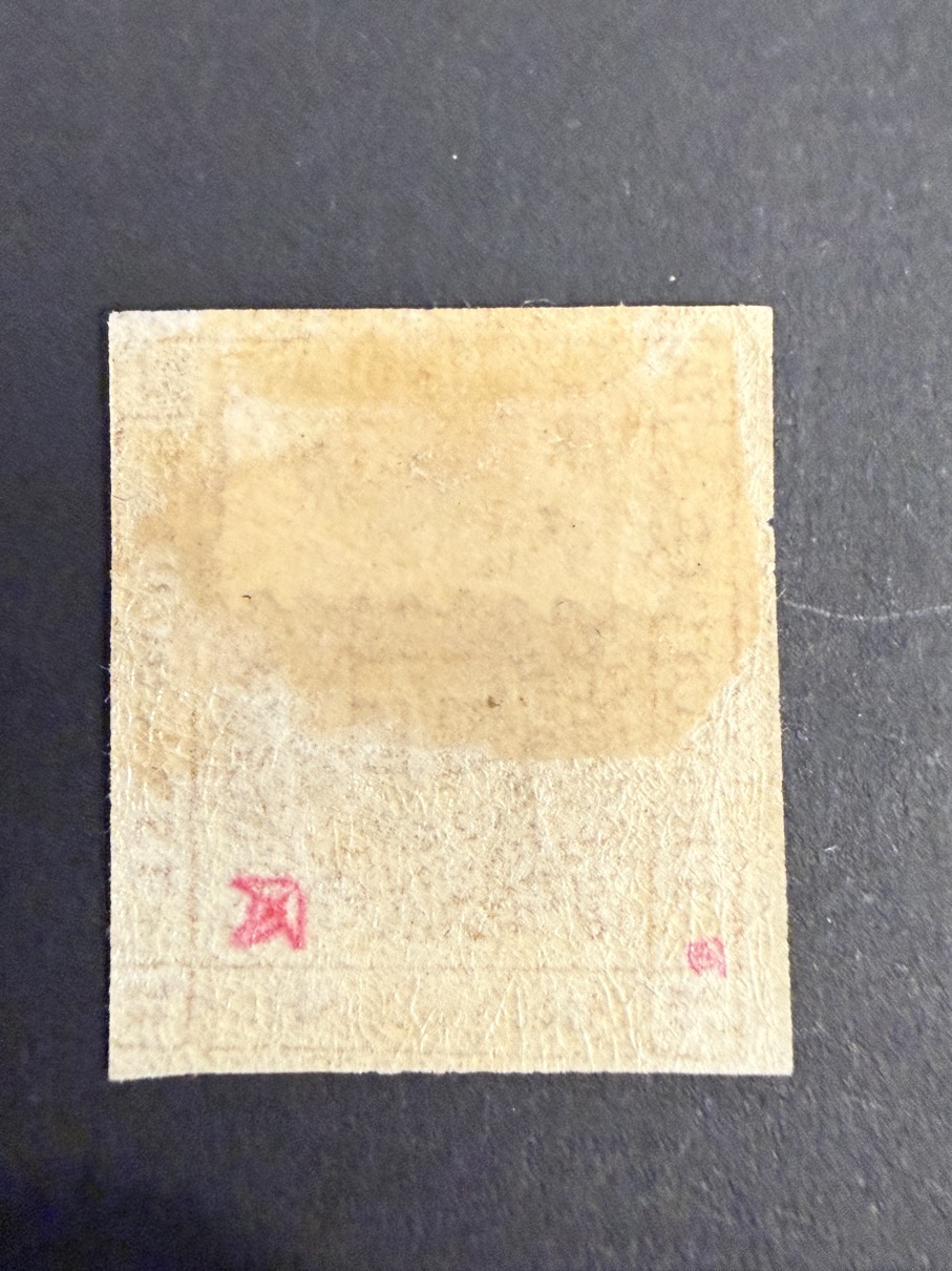 BM_1535_h - globalcollection.ch globalcollection.ch - Back side of a small beige square paper with rough edges and faint red corner marks on a dark surface.